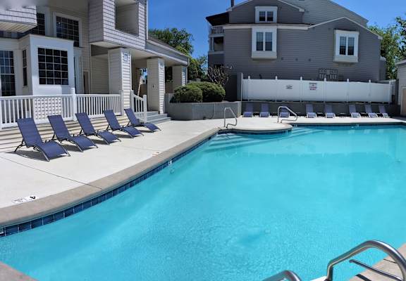 a swimming pool with blue chairs next to a house