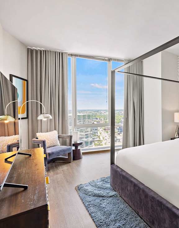 A large bed with a black frame in a room with a view of the city.