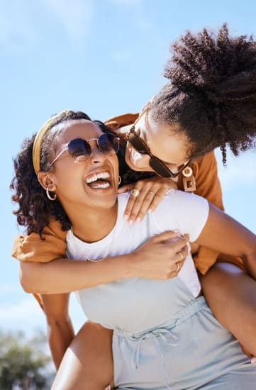 two women wearing sunglasses are laughing and having fun on a sunny day