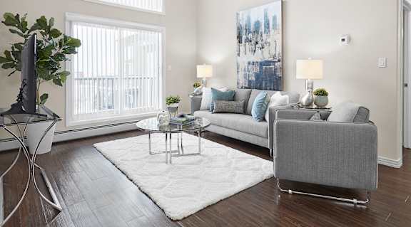 A living room with a grey couch, a glass table, and a large window.