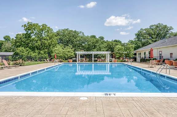 A large outdoor swimming pool surrounded by trees and a pavilion.
