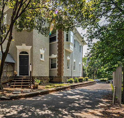 A white building with a black door is surrounded by trees.