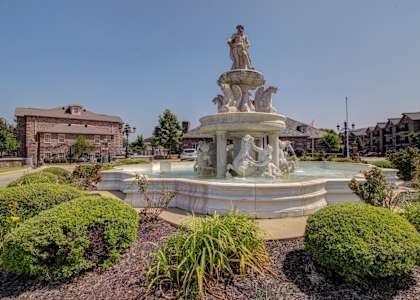 A fountain with a statue on top is surrounded by bushes.
