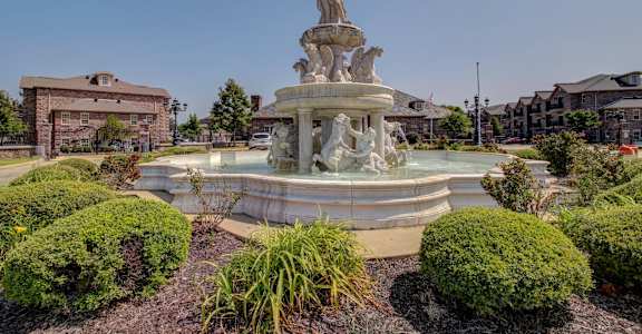 A fountain with a statue on top is surrounded by bushes.