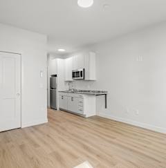 the living room and kitchen of an apartment with white walls and wood flooring