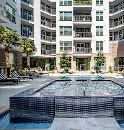 A large pool in the middle of a courtyard surrounded by lounge chairs and palm trees.