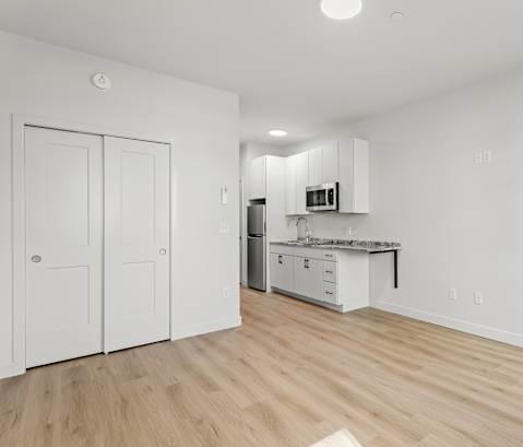 the living room and kitchen of an apartment with white walls and wood flooring
