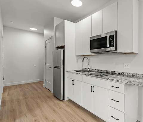 a kitchen with white cabinets and a counter top with a microwave and refrigerator
