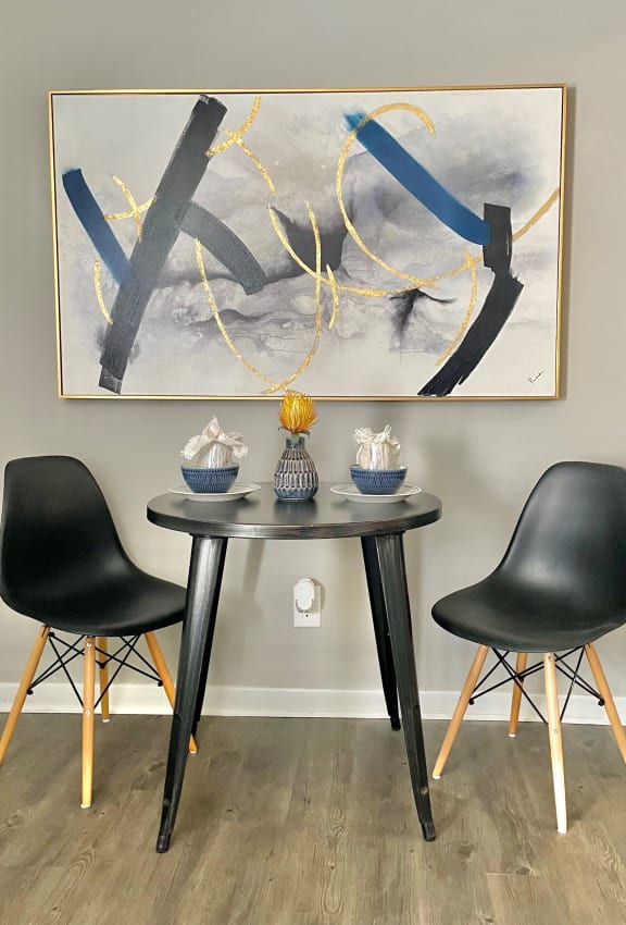 a dining table with two black chairs and a large painting on the wall