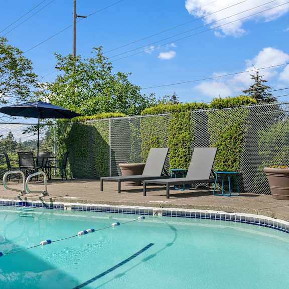 A pool with a diving board and lounge chairs.