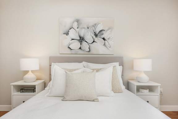 a bedroom with a bed with white pillows and a painting of flowers