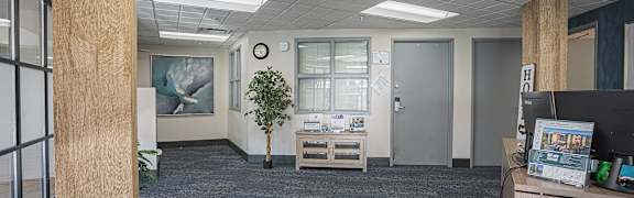 A room with a carpeted floor, a wooden pillar, a small table with a plant on it, and a wall with a clock.  at ParcOne60, Reno, 89501