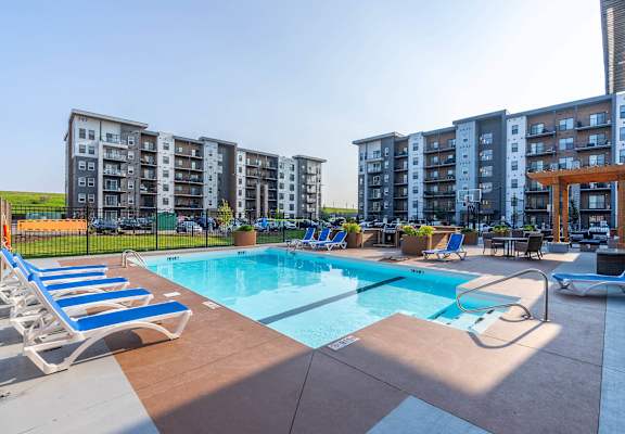 A swimming pool surrounded by sun loungers and chairs in front of apartment buildings at G17 Apartments at Tamarack, Edmonton, AB