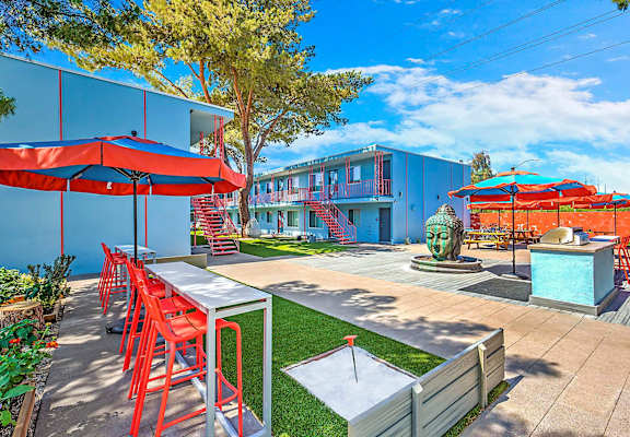 A patio with red chairs and tables is surrounded by a blue building.