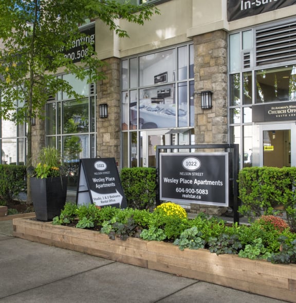 the front of a building with signs in front of plants