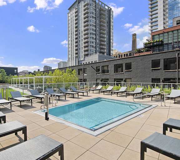 A pool surrounded by lounge chairs in a city setting.