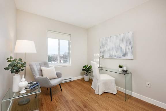 a living room with white walls and a glass desk with a chair and a window