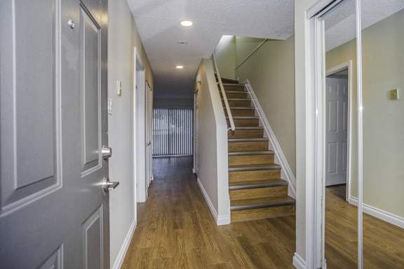a living room with a staircase and a hallway with wood floors and grey walls