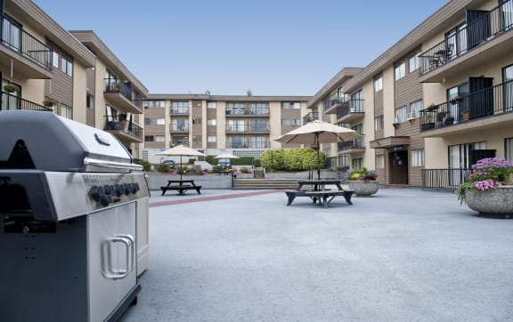 a large patio with a grill and picnic tables in front of an apartment building