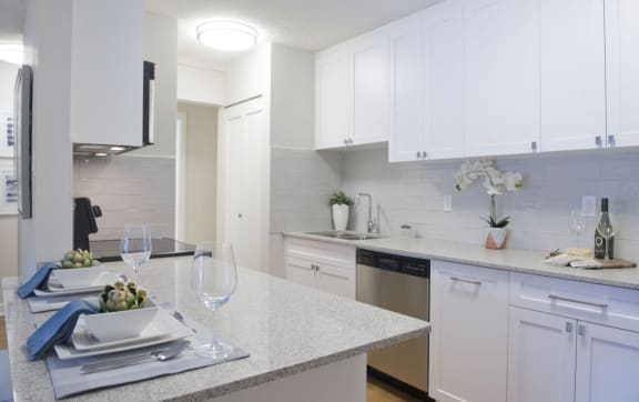 a kitchen with white cabinets and granite counter tops and a table with plates and glasses