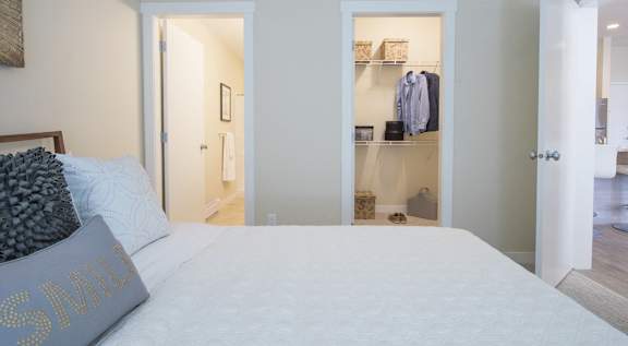A bedroom with a bed, a pillow, and a wall-mounted shelf with clothes.
