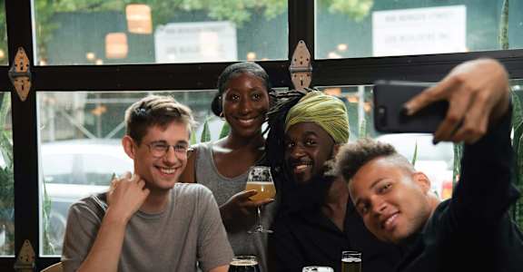 Four people are sitting at a table with drinks and taking a selfie.