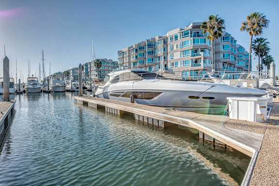 A yacht is docked at a marina with a building and palm trees in the background.