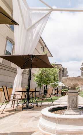 a fountain in the middle of a courtyard with tables and umbrellas at The Villa at River Pointe, Maumelle, AR