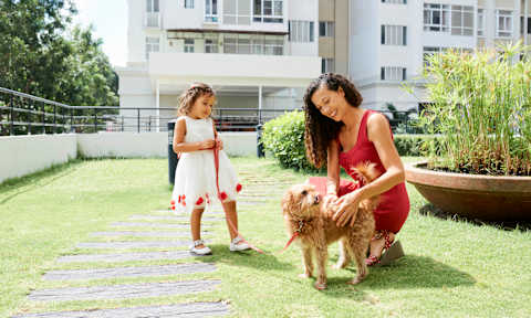 A woman and a little girl are playing with a dog in a garden.