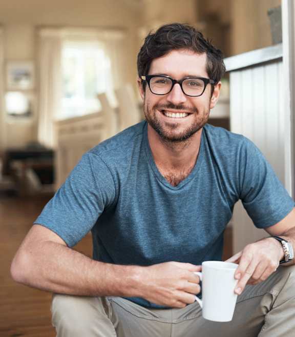 A man with glasses and a blue shirt is holding a white mug.