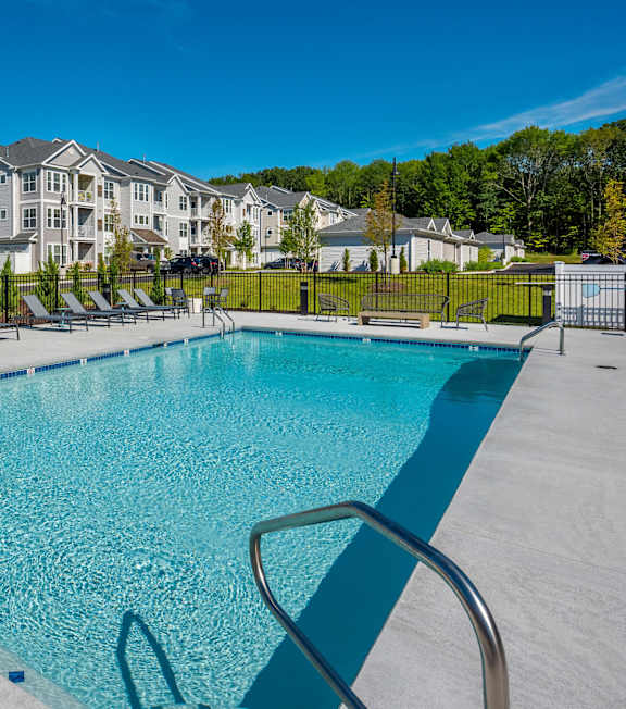 A swimming pool surrounded by lounge chairs and apartment buildings in the background.