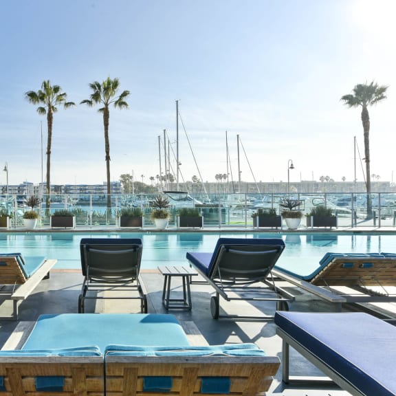 a pool with lounge chairs and tables and a marina  at Esprit Apartments, Marina del Rey, California