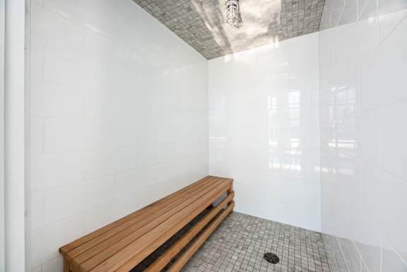 a large white tiled bathroom with a wooden bench