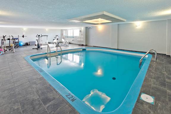 A swimming pool with a blue tint in a room with exercise equipment.