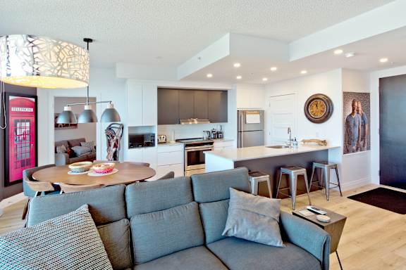 A modern living room with a grey couch and a kitchen in the background.