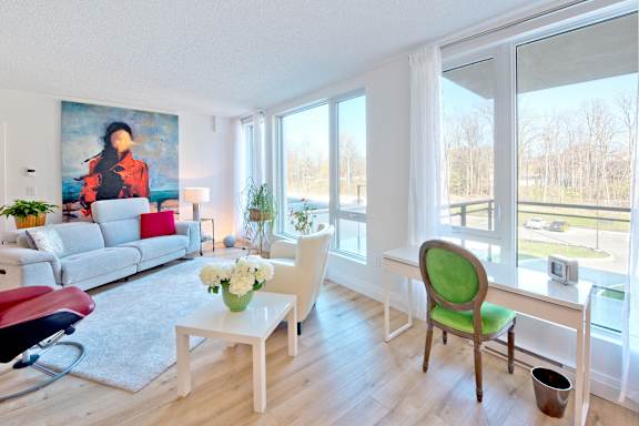 A living room with a white couch, a green chair, and a painting on the wall.