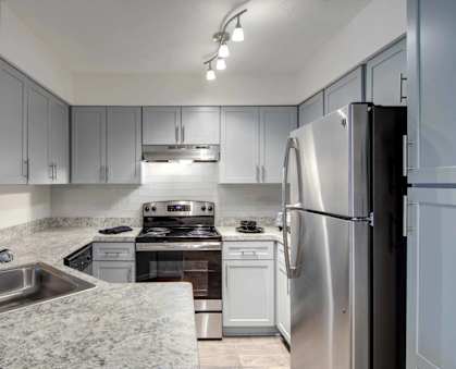 A modern kitchen with a stainless steel refrigerator and a sink with a marble countertop.