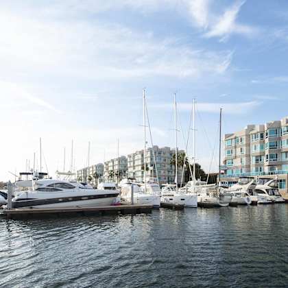 A yacht is docked at a marina with other boats and a building in the background.