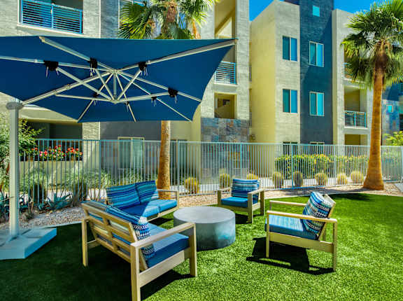 A blue umbrella shades a set of outdoor chairs. at Craft at Gilbert and Baseline Apartments, Apartments, Mesa, AZ