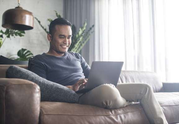 A man is sitting on a couch using a laptop.