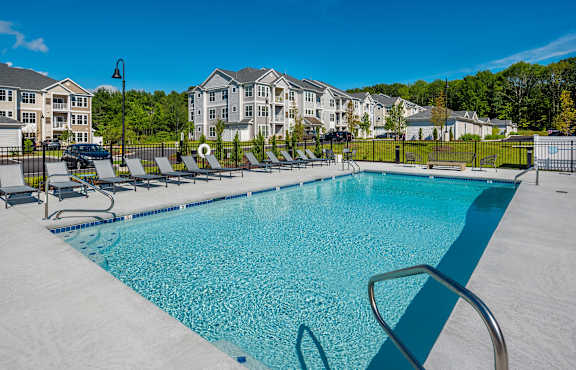 A swimming pool surrounded by lounge chairs and apartment buildings in the background.