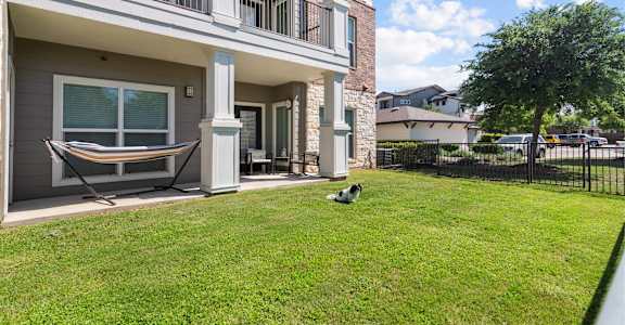 A dog is sitting on the grass in front of a two-story apartment building.