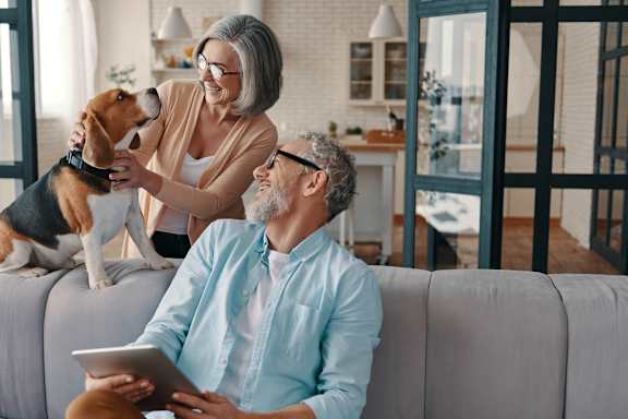 a man and woman sitting on a couch with a dog and a tablet