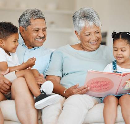 A family of four is sitting on a couch, reading a book together.