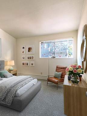 A bedroom with a bed, nightstand, chair, and a painting of a tree on the wall.