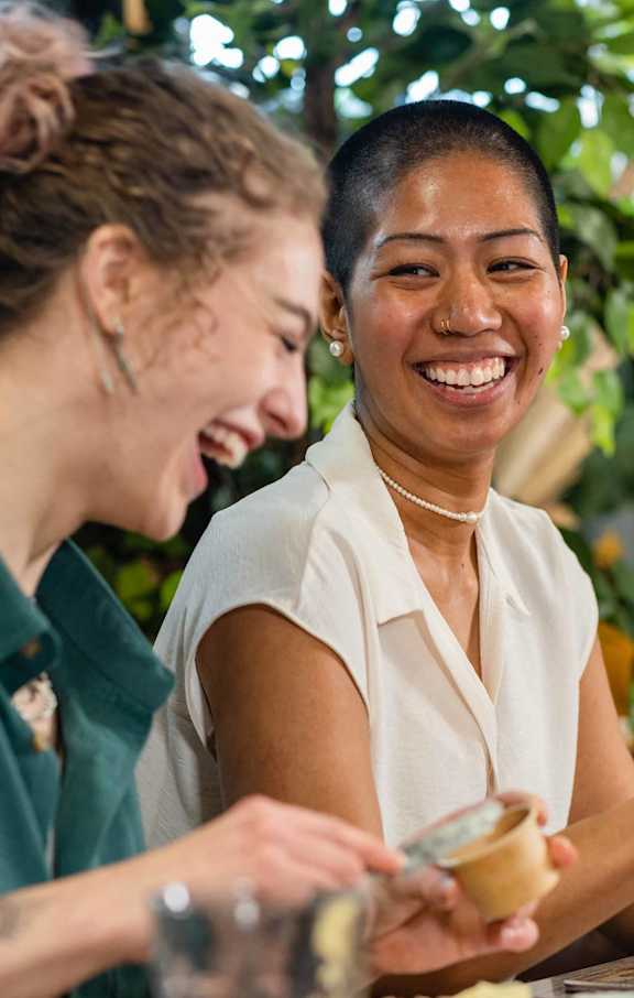 Two women laughing while eating food.