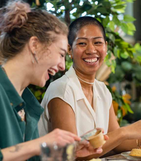 Two women laughing while eating food.