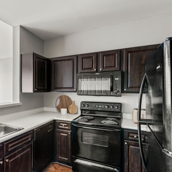 a kitchen with black appliances and dark wood cabinets at Veranda at Centerfield in Houston, Texas