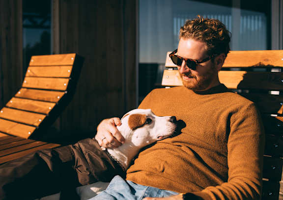 A woman is sitting on a couch holding a dog and looking at her phone.