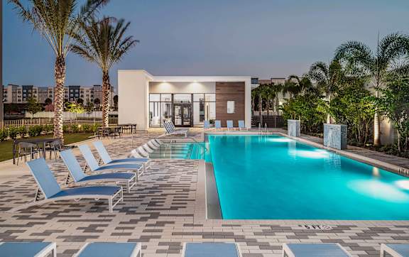 A pool surrounded by lounge chairs and palm trees.